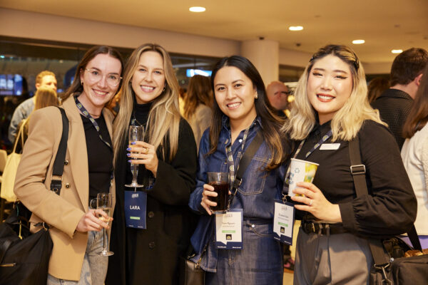 Four delegates with drinks and lanyards smile for the camera, State of Social ‘23